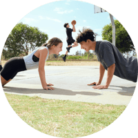 Young adult female and young adult female facing each other completing a pushup Young adult female and young adult female facing each other completing a pushup